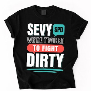 May include: Black t-shirt featuring the slogan "SEVY SPD WE'RE TRAINED TO FIGHT DIRTY" in white, red, and teal. The text is in a bold, modern font, suitable for everyday wear.