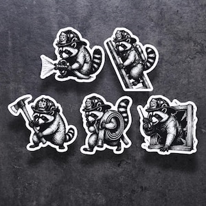 Puede incluir: Conjunto de cinco pegatinas en blanco y negro con mapaches de dibujos animados vestidos de bomberos. Cada mapache se representa en una acción de bombero diferente, como usar una manguera, subir una escalera o sostener un hacha.