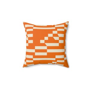 Op de afbeelding: Vierkant sierkussen met een geometrisch patroon in oranje en crème. Het ontwerp heeft horizontale en verticale lijnen en blokken, waardoor een gepixeleerd effect ontstaat. Het kussen heeft een vierkante vorm en lijkt van een zachte stof te zijn.