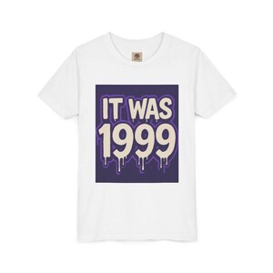 Puede incluir: Camiseta blanca con un gráfico cuadrado morado que dice "IT WAS 1999" en una fuente que gotea. La camiseta tiene cuello redondo y mangas cortas. El gráfico está centrado en la parte delantera.