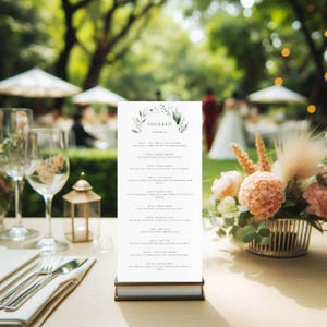 Könnte beinhalten: Eine Hochzeitsmenükarte mit den Namen "SAM & LIA" oben, umgeben von grünen Blättern. Das Menü wird auf einem Tisch mit Besteck, Gläsern und einem Blumenarrangement präsentiert. Der Hintergrund zeigt eine verschwommene Außenkulisse.