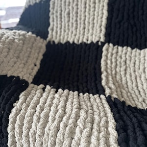 Può includere: Una coperta a quadri in maglia nera e bianca con una trama a maglia spessa.