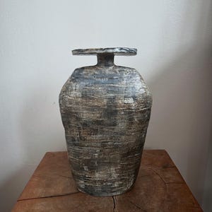 May include: A ceramic vase with a textured, gray and white glaze. The vase has a wide, round body and a flat, circular top.