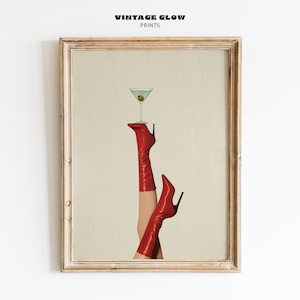 May include: Framed print featuring a martini glass with an olive, balanced on red high-heeled boots. The boots are knee-high and have black stiletto heels. The print is in a wooden frame, with the text "VINTAGE GLOW PRINTS" at the top.
