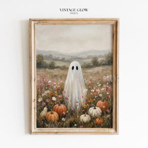 Könnte beinhalten: Ein gerahmter Kunstdruck mit dem Titel VINTAGE GLOW PRINTS, der ein Ölgemälde eines weißen Geistes in einem Feld mit Wildblumen und orangefarbenen Kürbissen unter einem bewölkten Himmel mit Hügeln im Hintergrund zeigt.