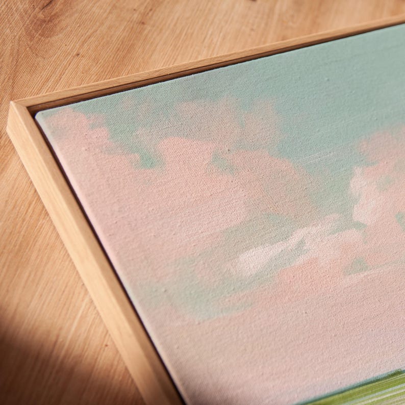 May include: A framed canvas artwork with a pastel landscape design. The painting uses soft pink, light blue, and green hues, set within a natural wood frame. The artwork creates a calm, airy feel, ideal for interior decoration.