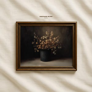 May include: A framed print featuring a still life of dried flowers in a dark pot. The artwork has a vintage aesthetic with a dark background and a gold-colored frame. The text "VINTAGE GLOW PRINTS" is at the top.