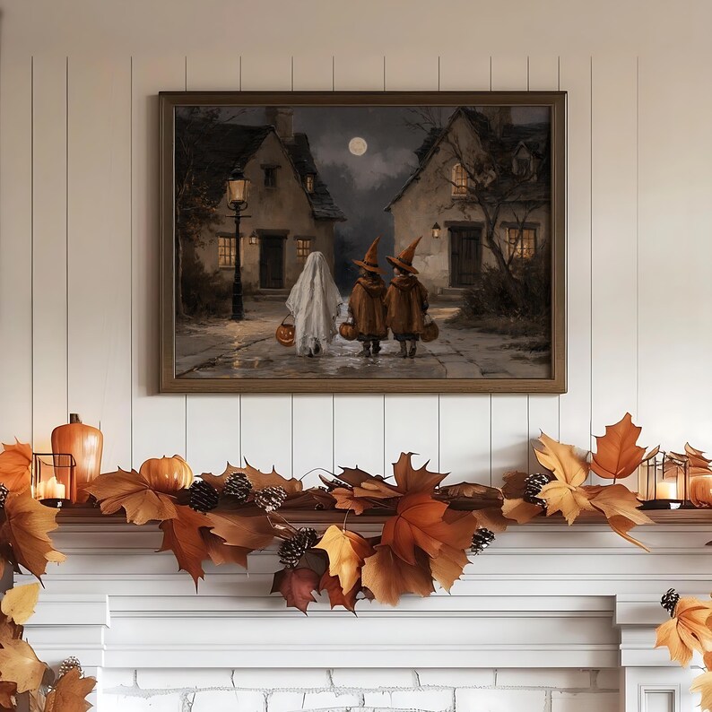 Op de afbeelding: Een ingelijste kunstdruk met een nachtelijke sc&egrave;ne van drie figuren die over een kasseienstraat tussen twee huizen lopen. E&eacute;n figuur draagt een wit spookkostuum, twee dragen oranje heksenhoeden en capes, en ze dragen allemaal pompoenen.