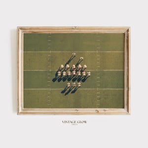 Może przedstawiać: Oprawiony wydruk przedstawiający widok z lotu ptaka na boisko do futbolu amerykańskiego z zawodnikami w strojach vintage. Zawodnicy ustawieni są w formacji na zielonym boisku, z widocznymi liniami jardów. Wydruk jest w drewnianej ramie, z tekstem "VINTAGE GLOW PRINTS" na dole.