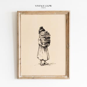 May include: A framed wall art print featuring a black ink line drawing on a cream background. The illustration depicts a person in a dress holding a tall stack of books that obscures their face. The text VINTAGE GLOW PRINTS appears at the top.