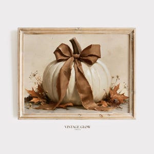 Puede incluir: Una impresión artística enmarcada que presenta una pintura al óleo de una calabaza blanca atada con un gran lazo marrón. La calabaza está rodeada de hojas de otoño secas y ramitas, sobre un fondo neutro de color claro.