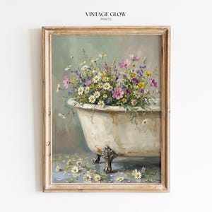 Puede incluir: Una impresión enmarcada de estilo vintage que representa una bañera con patas de garra rebosante de coloridas flores silvestres. La obra de arte tiene una calidad suave y pictórica con una paleta de colores apagados de blanco, rosa, morado y verde. El texto "VINTAGE GLOW PRINTS" está en la parte superior.