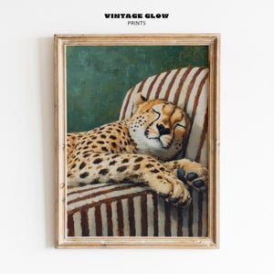 May include: A framed print featuring a sleeping cheetah on a striped armchair. The cheetah has a tan coat with black spots. The chair has brown and white stripes. The background is a dark green color. The text "VINTAGE GLOW PRINTS" is at the top.