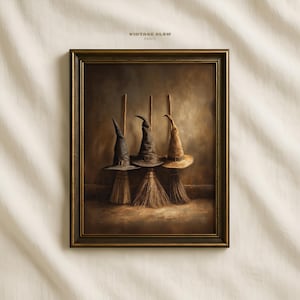 Puede incluir: Una impresión enmarcada que presenta tres sombreros de bruja sobre escobas. Los sombreros son en tonos negro, gris y beige, con hebillas. Las escobas son de paja. La impresión tiene una estética vintage, en tonos sepia, con el texto "VINTAGE GLOW PRINTS" en la parte superior.