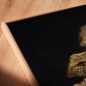 K&ouml;nnte beinhalten: Ein gerahmtes Wandbild mit einer detaillierten, realistischen Illustration eines menschlichen Sch&auml;dels vor einem einfarbigen schwarzen Hintergrund. Das Kunstwerk ist in einen hellen Holzrahmen mit schlichter Kante gefasst, der den Kontrast zwischen dem dunklen Inneren und der nat&uuml;rlichen Holzmaserung des Rahmens betont.