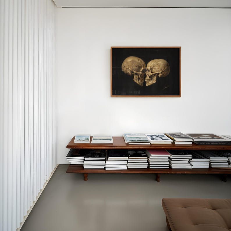 K&ouml;nnte beinhalten: Ein rechteckiges, zweist&ouml;ckiges B&uuml;cherregal aus Holz, das mit zahlreichen gestapelten B&uuml;chern gef&uuml;llt ist. &Uuml;ber dem Regal befindet sich ein gerahmtes, horizontales Kunstwerk mit zwei beigen menschlichen Sch&auml;deln vor schwarzem Hintergrund.