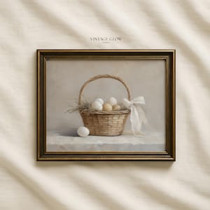 Può includere: Stampa incorniciata raffigurante un cesto di vimini pieno di uova ed erba secca. Un nastro bianco è legato al manico del cesto. La stampa ha un'estetica vintage, con il testo "VINTAGE GLOW PRINTS" in alto.