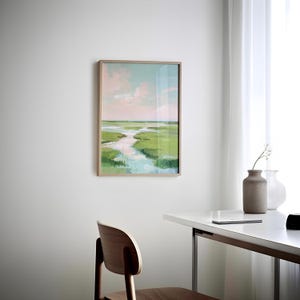 May include: A framed landscape painting of a marsh scene with a winding waterway. The artwork uses green, blue, and pink hues, with a light brown wooden frame. The painting is displayed on a white wall.