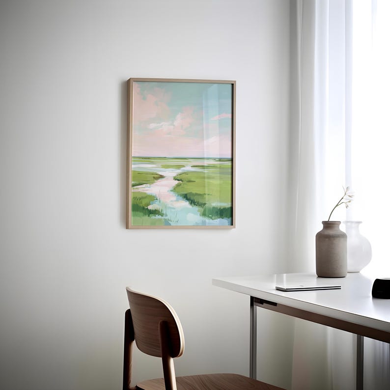 May include: A framed landscape painting of a marsh scene with a winding waterway. The artwork uses green, blue, and pink hues, with a light brown wooden frame. The painting is displayed on a white wall.