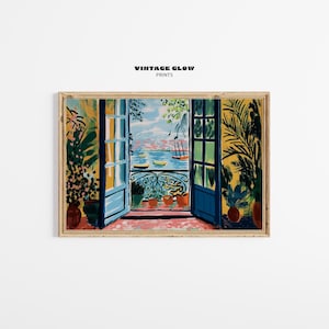 May include: A framed art print depicting an open doorway overlooking a seascape. The artwork features blue doors, potted plants, and a balcony with boats on the water. The text "VINTAGE GLOW PRINTS" is at the top.