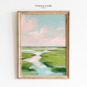 May include: Framed landscape art print depicting a marsh scene with a light blue sky and pink clouds. The artwork has a gold-coloured frame and the text "VINTAGE GLOW PRINTS" at the top.