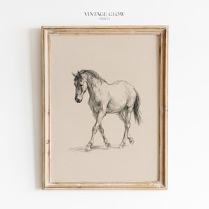 May include: A framed wall art print featuring a charcoal pencil sketch of a horse walking on a beige background. The text VINTAGE GLOW PRINTS is centered at the top. The frame is made of light-colored wood with a weathered, textured finish.