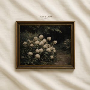 May include: A framed vintage print featuring a dark, moody landscape with white hydrangea blooms. The artwork has a gold-toned frame and the text "VINTAGE GLOW PRINTS" at the top. The painting depicts a path through a garden.