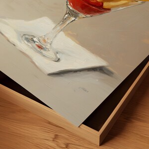 Pode incluir: Pintura a &oacute;leo de um cocktail num copo com p&eacute;, com uma bebida vermelha e amarela. O copo repousa sobre um guardanapo branco, sobre um fundo neutro. A obra de arte &eacute; emoldurada numa moldura de madeira clara.