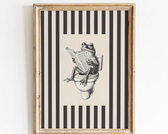May include: Framed art print featuring a frog reading a newspaper while seated on a toilet. The artwork is in black and white, set against a striped background of black and beige. The frame is a light brown color. The text "VINTAGE GLOW PRINTS" is at the top.