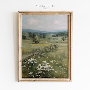 Puede incluir: Pintura de paisaje enmarcada que presenta una escena de pradera serena con un camino sinuoso, una valla de madera y un edificio distante con techo rojo. La obra de arte muestra un campo de flores silvestres y exuberante vegetación bajo un cielo nublado. El marco es de madera clara y envejecida.
