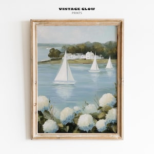 May include: A framed painting depicts a serene coastal scene. Three white sailboats glide on a light blue body of water, with white buildings and green trees in the background. The foreground features white and blue hydrangeas. The text "VINTAGE GLOW PRINTS" is at the top.