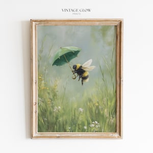 May include: A framed print featuring a whimsical illustration of a bumblebee holding a small green umbrella, flying over a field of tall green grass and wildflowers. The artwork has a vintage aesthetic, with soft colors and a dreamy quality. The text "VINTAGE GLOW PRINTS" is at the top.