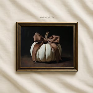 May include: A framed wall art print featuring a white pumpkin tied with a large brown ribbon against a dark background. The text VINTAGE GLOW PRINTS is visible at the top center. The artwork is enclosed in a dark, metallic-toned rectangular frame.