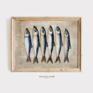 以下が含まれることがあります： ニュートラルな背景に、青と白の6匹の様式化された魚が描かれた額入りのプリント。アートワークは明るい色の木製フレームに収められています。「VINTAGE GLOW PRINTS」の文字が画像の下部にあります。
