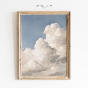 May include: A framed wall art print featuring a painting of fluffy white cumulus clouds against a soft blue sky. The rectangular frame is made of light brown wood with a weathered texture. The text VINTAGE GLOW PRINTS is centred above the frame.