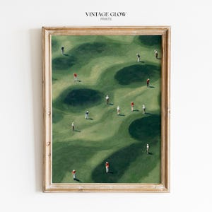 Könnte beinhalten: Ein gerahmter Kunstdruck mit dem Titel VINTAGE GLOW PRINTS zeigt eine Luftaufnahme eines Golfplatzes mit hügeligen grünen Flächen, dunklen Sandbunkern und kleinen Figuren von Golfspielern in rot-weiß-blauer Kleidung auf dem Gelände.