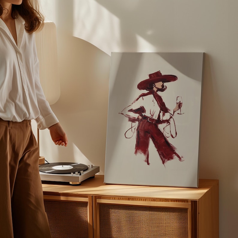 Puede incluir: Impresi&oacute;n en lienzo de una ilustraci&oacute;n de moda que representa a una persona con sombrero de ala ancha, bufanda y pantal&oacute;n burdeos, sosteniendo una copa de vino. La obra de arte est&aacute; sobre un fondo neutro, con una paleta de colores c&aacute;lidos.