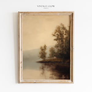 Può includere: Una stampa incorniciata di un paesaggio con una serena scena lacustre con alberi lungo la riva. L'opera d'arte ha un'estetica vintage con colori tenui e tenui e una superficie d'acqua riflettente. Il testo "VINTAGE GLOW PRINTS" è in alto.