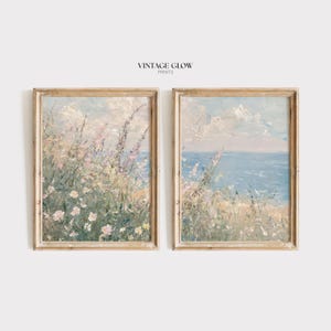 Pode incluir: Duas pinturas de paisagem emolduradas. A obra de arte retrata uma cena costeira com flores silvestres e vistas para o oceano. As pinturas estão em molduras de madeira clara. O texto "VINTAGE GLOW PRINTS" está no topo.
