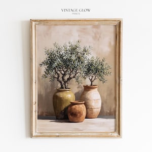 May include: A framed wall art print titled VINTAGE GLOW PRINTS featuring an oil painting of two olive trees in three terracotta and ceramic pots. The trees have green leaves and small dark olives, set against a neutral beige textured background.