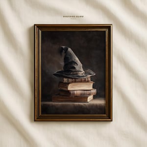 May include: A framed print featuring a wizard's hat atop a stack of old books. The hat is dark gray, and the books are bound in brown leather. The frame is a dark gold color, and the text "VINTAGE GLOW PRINTS" is at the top.