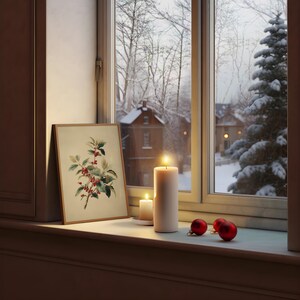 May include: A cozy winter scene featuring a framed botanical print of holly berries, two lit candles, and red ornaments on a windowsill. The window overlooks a snowy landscape with houses and trees, creating a warm, inviting atmosphere.