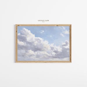 Könnte beinhalten: Ein gerahmter Druck mit einem bewölkten Himmel in Blau-, Weiß- und Grautönen. Das Kunstwerk befindet sich in einem rechteckigen, hellbraunen Holzrahmen. Der Text "VINTAGE GLOW PRINTS" steht oben.