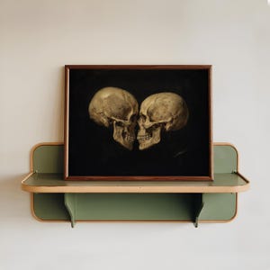K&ouml;nnte beinhalten: Ein rechteckiger gerahmter Druck mit zwei menschlichen Sch&auml;deln, die sich vor einem einfarbigen schwarzen Hintergrund gegen&uuml;berstehen. Die Sch&auml;del sind in Beige- und Cremet&ouml;nen gehalten. Das Kunstwerk befindet sich in einem dunkelbraunen Holzrahmen.