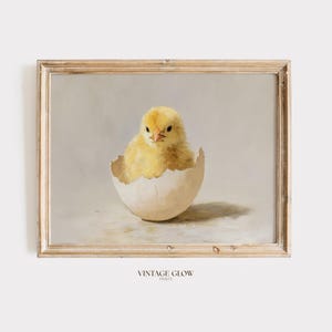 May include: A framed print featuring a yellow chick emerging from a cracked eggshell. The chick is fluffy and detailed, set against a soft, neutral background. The frame is light-colored wood, and the print has a vintage aesthetic.