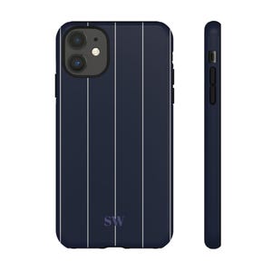 May include: Navy blue phone case with vertical white stripes. The case has a sleek design and features a camera cutout and side buttons. The initials "SW" are at the bottom. The case is shown from the front and side.