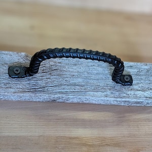 May include: Black metal handle with a twisted design, mounted on a piece of weathered wood.