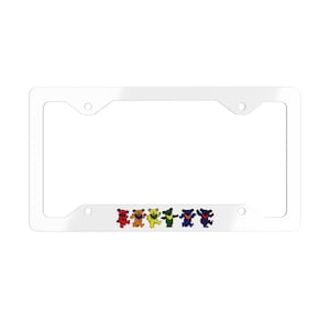 May include: White license plate frame featuring a row of dancing bears in red, orange, yellow, green, blue, and purple. The bears have a cheerful expression and are in a line. The frame has a rectangular shape.
