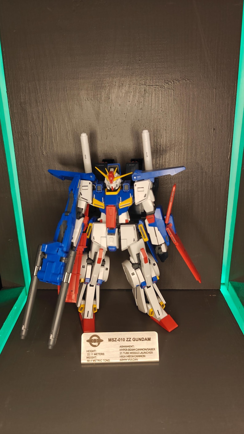 May include: A detailed model of the MSZ-010 ZZ Gundam, a mecha robot, in a display. The robot is primarily white, blue, and red, with a detailed design. The model includes a beam saber and missile launcher. The text on the display reads "MSZ-010 ZZ GUNDAM".