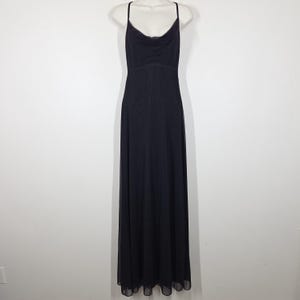 May include: A floor-length black dress featuring a cowl neckline, thin spaghetti straps, and a fitted bodice that transitions into a flowing, sheer-layered skirt. The garment is displayed on a mannequin, showcasing a simple, elegant silhouette.